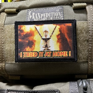 Op de afbeelding: Een zwart en grijs patch met een gele en oranje afbeelding van een brandende stroomlijn. De tekst "I TRIED IT AT HOME!" is in wit op de patch gedrukt.