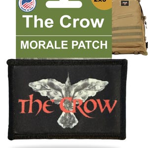 May include: A black morale patch with a white crow design and the words "The Crow" in red. The patch measures 2x3 inches and is displayed with a tan backpack.