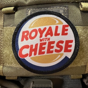 May include: A black and white patch with a red and white logo that says "Royale with Cheese" on a green fabric background.