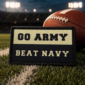 May include: A rectangular patch with a black border featuring a two-tone design. The top half is tan with the text GO ARMY in black, and the bottom half is black with the text BEAT NAVY in tan. The patch is positioned on a green grass field.