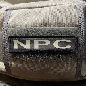 May include: A close-up of a gray tactical bag with a black patch that reads "NPC" in white letters.