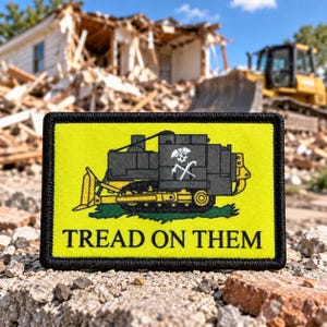 May include: A rectangular embroidered patch with a bright yellow background and a black border. It features a graphic of a dark gray bulldozer with a white skull and crossbones emblem on its side. The text TREAD ON THEM is printed in black.