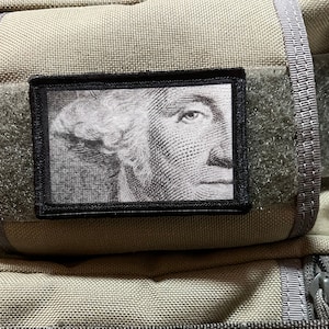 May include: A black and white patch with a close-up image of George Washington's face on a beige background.
