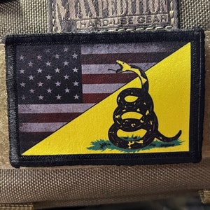 May include: A black and yellow patch with a stylized image of a snake coiled around a yellow background with a red and white American flag in the background. The snake is black and has a white tongue. The text "Don't Tread On Me" is printed on the snake.