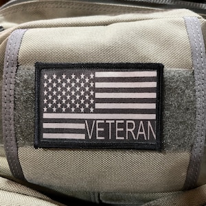 May include: A gray tactical bag with a black patch featuring a white American flag and the word "VETERAN".