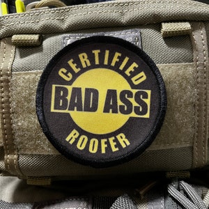 May include: A black and yellow patch with the text "CERTIFIED BAD ASS ROOFER" on a green bag.