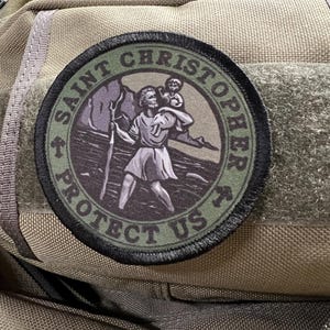 May include: A green and black embroidered patch with a saint carrying a child. The patch reads "Saint Christopher Protect Us".