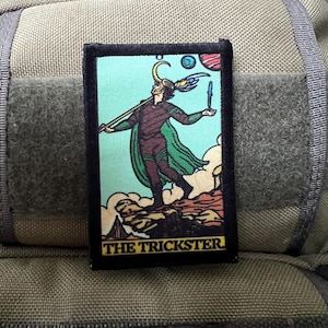 May include: A black and green embroidered patch with a cartoon image of a character holding a staff and a dagger. The background is a light blue color with clouds and a red and blue planet. The text "THE TRICKSTER" is printed in yellow at the bottom of the patch.