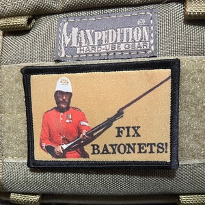 Puede incluir: Un parche blanco y negro con una imagen de dibujos animados de un soldado con un uniforme rojo sosteniendo un rifle. El texto "FIX BAYONETS!" está impreso debajo de la imagen.