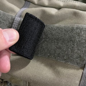 Pode incluir: Close-up de um fecho de velcro preto preso a uma superf&iacute;cie de tecido bege. O fecho de velcro &eacute; feito de um material tecido e tem uma textura &aacute;spera.