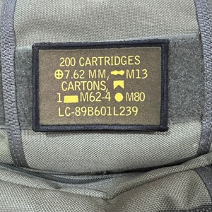 May include: A green military-style pouch with a yellow patch that reads "200 CARTRIDGES 7.62 MM, M13 CARTONS, M62-4 M80 LC-89B601L239".