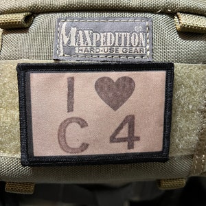 Puede incluir: Un parche de color beige y negro con el texto "I ♥ C4" y el logotipo "Maxpedition Hard-Use Gear" encima.
