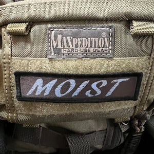 May include: A green and brown backpack with a black strap and a patch that says "Maxpedition Hard-Use Gear" and another patch that says "MOIST".