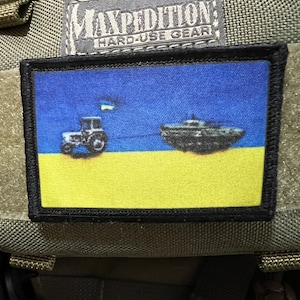 May include: A black and yellow patch with a blue background. The patch features a tractor and a boat, both in black, on a yellow field. The text "EXPEDITION HARD-USE GEAR" is visible on the top of the patch.