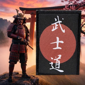 Op de afbeelding: Een rechthoekige zwarte geborduurde patch met een grote rode cirkel in het midden. Over de rode cirkel staan drie witte Japanse kanji-tekens verticaal gerangschikt. De patch heeft een dikke zwarte gestikte rand rondom de zijkanten.