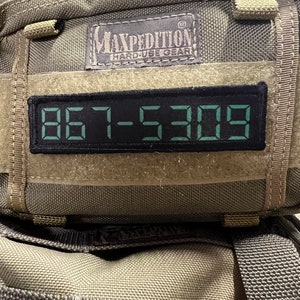 May include: A green and black Maxpedition Hard Use Gear backpack with a black velcro patch that reads "867-5309".