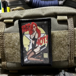May include: A black patch with a red, white, and yellow cartoon image of a woman with red hair and a black outfit. The text "RED HOT!" is on the patch.