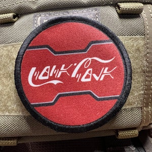 May include: A red and black circular patch with a white stylised logo that says "WALK'N'TALK" on a green fabric background.