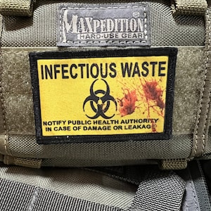 May include: A black and yellow patch with the text "INFECTIOUS WASTE" and a biohazard symbol. The text "NOTIFY PUBLIC HEALTH AUTHORITY IN CASE OF DAMAGE OR LEAKAGE" is below the symbol.