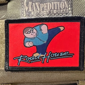 May include: A black and red embroidered patch with a cartoon illustration of a man in a blue shirt and jeans kicking with the text "Road House" in blue cursive.
