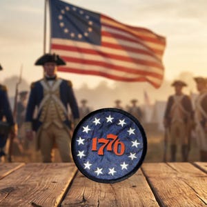 May include: A circular embroidered patch featuring a dark blue background with a ring of thirteen white stars surrounding the orange-red text 1776. The patch is positioned on a wooden surface with a blurred historical military scene in the background.
