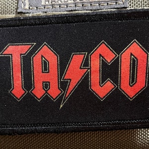 May include: A black patch with a red "TACO" logo in a stylized font with a lightning bolt between the "A" and "C".