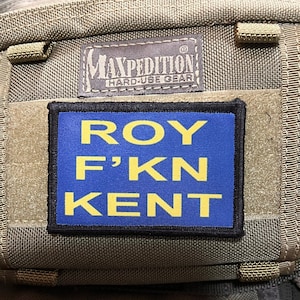 Pode incluir: Um remendo azul e amarelo com o texto "ROY F'KN KENT" em uma bolsa marrom Maxpedition Hard Use Gear.