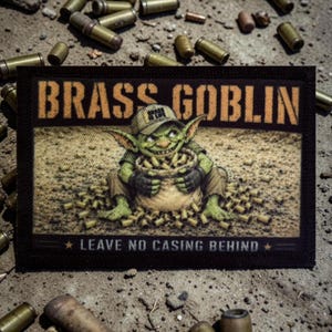 Op de afbeelding: Een rechthoekige patch met de woorden "BRASS GOBLIN" in oranje blokletters. De patch toont een groene goblin die een zak met messing hulzen vasthoudt. De tekst "LEAVE NO CASING BEHIND" staat eronder.