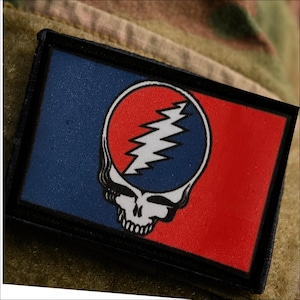May include: A rectangular patch featuring a split blue and red background with a central graphic of a skull with a lightning bolt design. The skull is white with black outlines, and the lightning bolt is white set against a blue circular field.