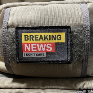 May include: A black patch with white stitching and the text "BREAKING NEWS I DON'T CARE" in yellow and red letters.