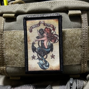 May include: A black and white patch with a mermaid holding an anchor. The mermaid has red hair and a blue tail. The patch has the text "Lost at Sea" on a banner above the mermaid.