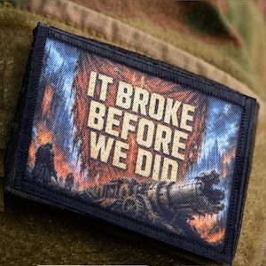 May include: A rectangular morale patch with a black border featuring a vibrant, fiery background with orange and blue flames. The text IT BROKE BEFORE WE DID is printed in bold, light-colored capital letters across the center of the patch.