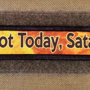 May include: A black and yellow patch with the text "Not Today, Satan" on a textured brown background.