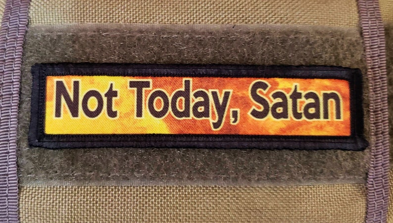 May include: A black and yellow patch with the text "Not Today, Satan" on a textured brown background.