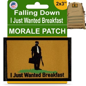 May include: A 2x3 inch morale patch with a black silhouette of a person holding a briefcase and a gun. The patch is brown with green grass at the bottom and the text "I Just Wanted Breakfast" in black.
