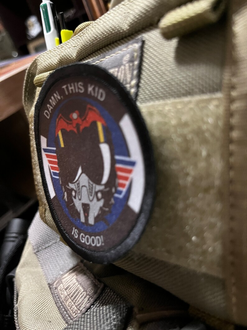 May include: A beige fabric bag with a patch that reads "DAMN THIS KID IS GOOD!" The patch features a cartoon pilot wearing a helmet and goggles.