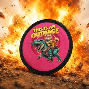 May include: A circular embroidered patch with a black border on a bright pink background. The design features a fluffy orange cat wearing purple sunglasses riding a green dinosaur. The text THIS IS AN OUTRAGE is printed in yellow above the cat.