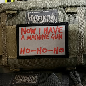 Könnte beinhalten: Eine grüne Maxpedition Hard-Use Gear Tasche mit einem Patch, auf dem "NOW I HAVE A MACHINE GUN HO-HO-HO" steht.