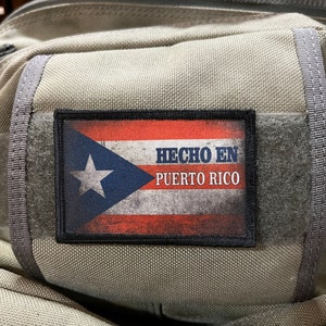 May include: A gray backpack with a black patch featuring the Puerto Rican flag and the text "Hecho en Puerto Rico".