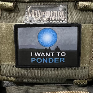 Könnte beinhalten: Ein schwarzer Patch mit einem blauen Kreis und dem Text "I WANT TO PONDER" auf einer grünen Maxpedition-Tasche.