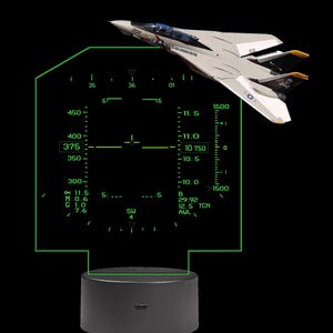 May include: A decorative light featuring a fighter jet model positioned above a flat, transparent acrylic panel etched with a green digital heads-up display interface. The display shows various flight data metrics, numbers, and symbols.