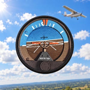 Può includere: Una toppa ricamata circolare che raffigura uno strumento indicatore di assetto aeronautico. Il design mostra un cielo blu, una linea dell'orizzonte marrone, barre di beccheggio arancioni, segni bianchi e il testo SIGMA-TEK su bordo nero.