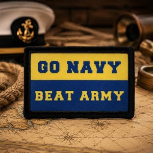 Puede incluir: Un parche rectangular bordado con un borde negro. La mitad superior es amarilla con el texto GO NAVY en azul, y la mitad inferior es azul con el texto BEAT ARMY en amarillo. El parche presenta un diseño limpio, audaz y letras claras.