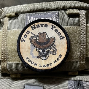 May include: A beige and black embroidered patch with a skull wearing a cowboy hat and the text "You Have Yee'd Your Last Haw".