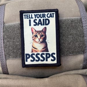 Puede incluir: Un parche blanco y negro con un gato atigrado marrón y el texto "Tell your cat I said PSSSSS"