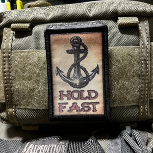 May include: A black and white anchor with a rope design on a tan background. The text "HOLD FAST" is in red letters below the anchor.