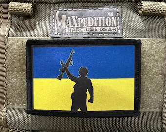 Puede incluir: Un parche negro con una bandera ucraniana amarilla y azul y una silueta de una persona sosteniendo un rifle. El texto "Maxpedition Hard-Use Gear" es visible en la bolsa.