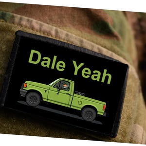 Puede incluir: Un parche negro con el texto "Dale Yeah" en verde. Debajo, una ilustración de una camioneta verde con un conductor. El parche está sobre un fondo de camuflaje.