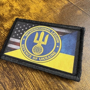 May include: A black patch with a yellow and blue Ukrainian flag and a circular emblem with the text "International Legion Defence of Ukraine" in gold lettering. The emblem features a trident and a globe.