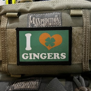 Peut inclure: Un patch vert et noir avec le texte "I love Gingers" et un cœur avec un trèfle à quatre feuilles à l'intérieur. Le patch est fixé à un sac vert Maxpedition Hard-Use Gear.